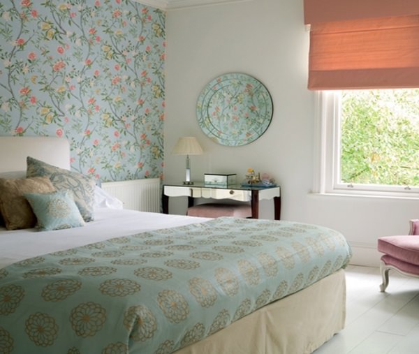 اتاق خواب با تخت دونفره و دیوارهای سفید رنگ که روی دیوار پشتی آن کاغذ دیواری آبی با طرح گل نصب شده است